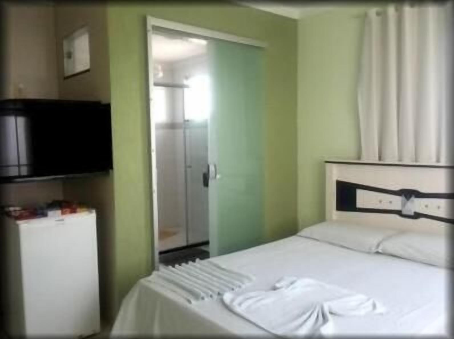 A hotel room with a bed, a small white desk, a television, and a door leading to a bathroom.