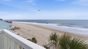 A beach view with a seagull flying, a sandy beach, and a building with a balcony. - OD 2103C Top Floor Oceanfront Condo, elevator, Indoor/Outdoor Pools (Kure Beach)