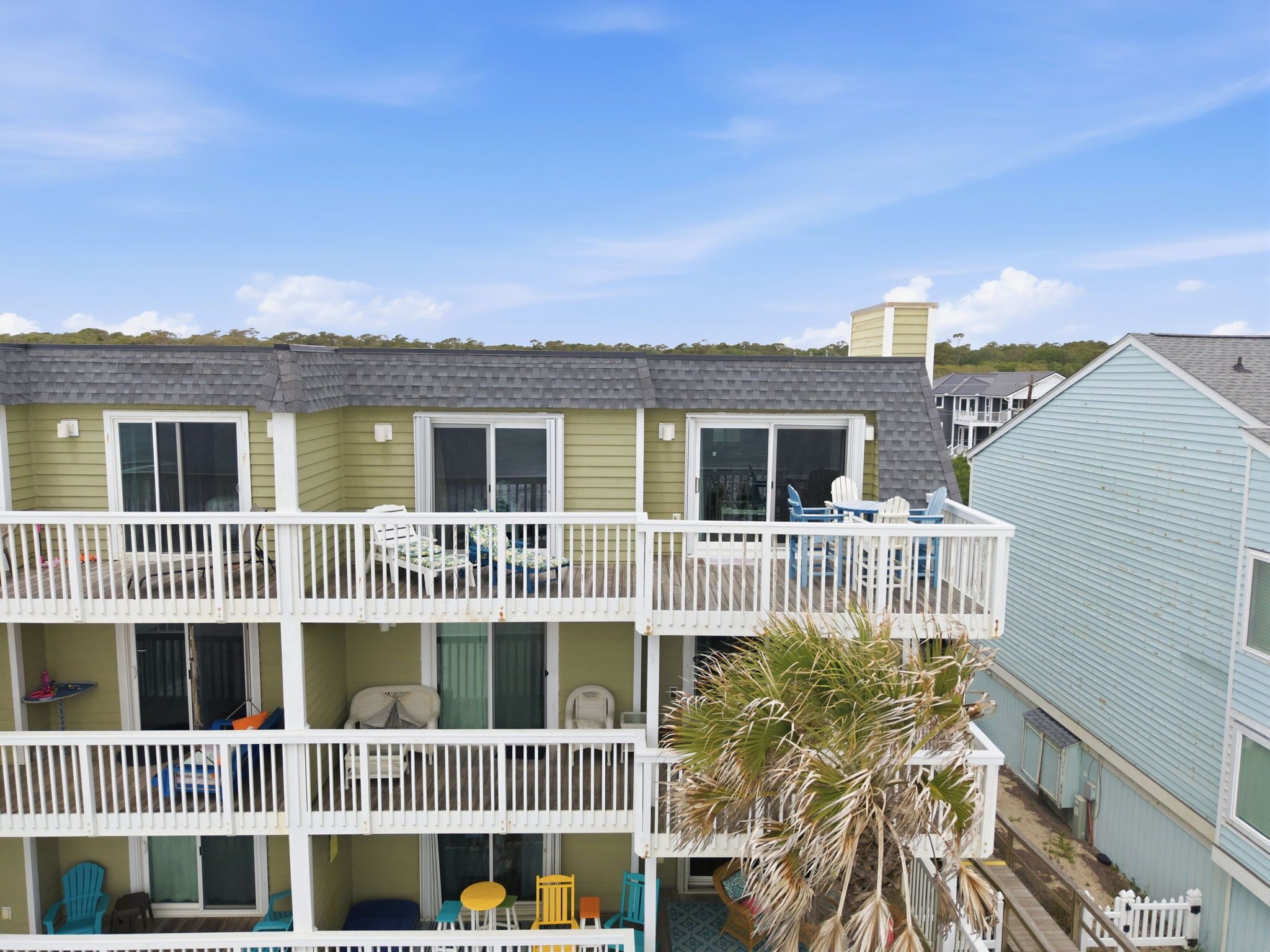 A multi-story building with balconies, outdoor seating, and a palm tree.