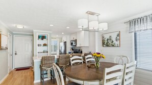 A dining area with a round table, white chairs, and a vase of flowers. - OD 2103C Top Floor Oceanfront Condo, elevator, Indoor/Outdoor Pools (Kure Beach)