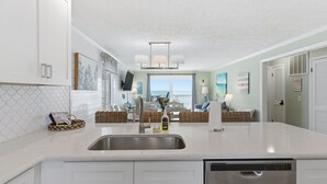 A kitchen with a large island, stainless steel sink, and white cabinetry. - OD 2103C Top Floor Oceanfront Condo, elevator, Indoor/Outdoor Pools (Kure Beach)