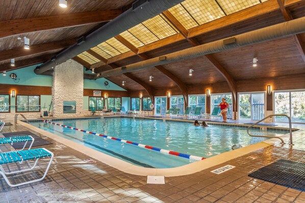 Une piscine intérieure avec des couloirs clairement délimités, un pilier en pierre et une vue sur l’extérieur grâce à de grandes fenêtres.