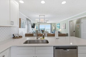 A kitchen with a large island, stainless steel sink, and white cabinetry. - OD 2103C Top Floor Oceanfront Condo, elevator, Indoor/Outdoor Pools (Kure Beach)