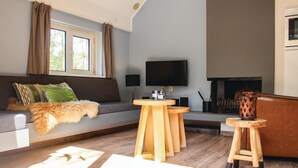 Olohuoneessa on sohva, kaksi puista jakkaraa, televisio ja takka.
