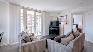 Una sala de estar moderna con dos sofás, un televisor sobre un mueble negro y un ventanal con vistas a la ciudad.