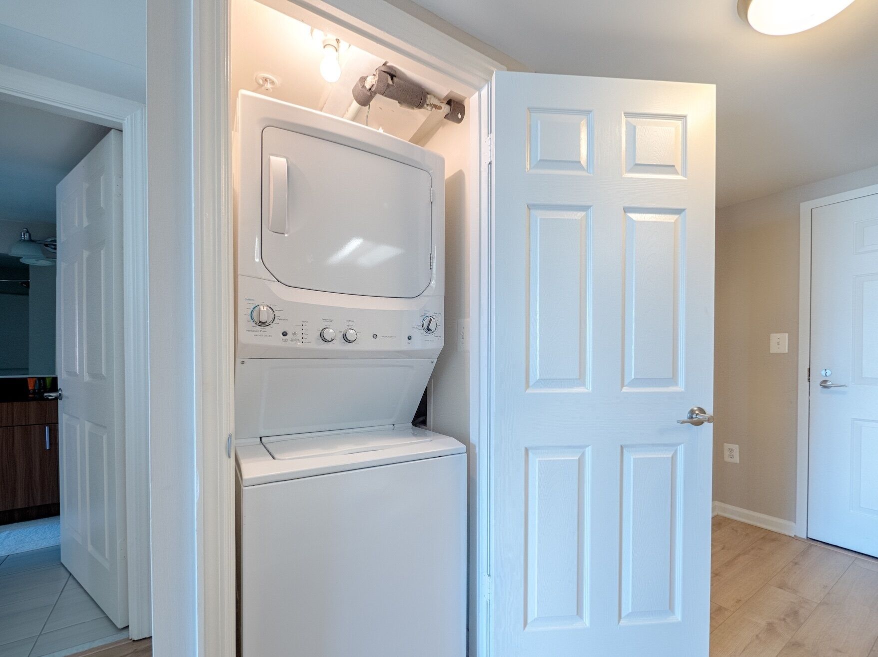 Une buanderie équipée d’un lave-linge et d’un sèche-linge superposés, d’une porte blanche et d’un luminaire placé au-dessus du sèche-linge.