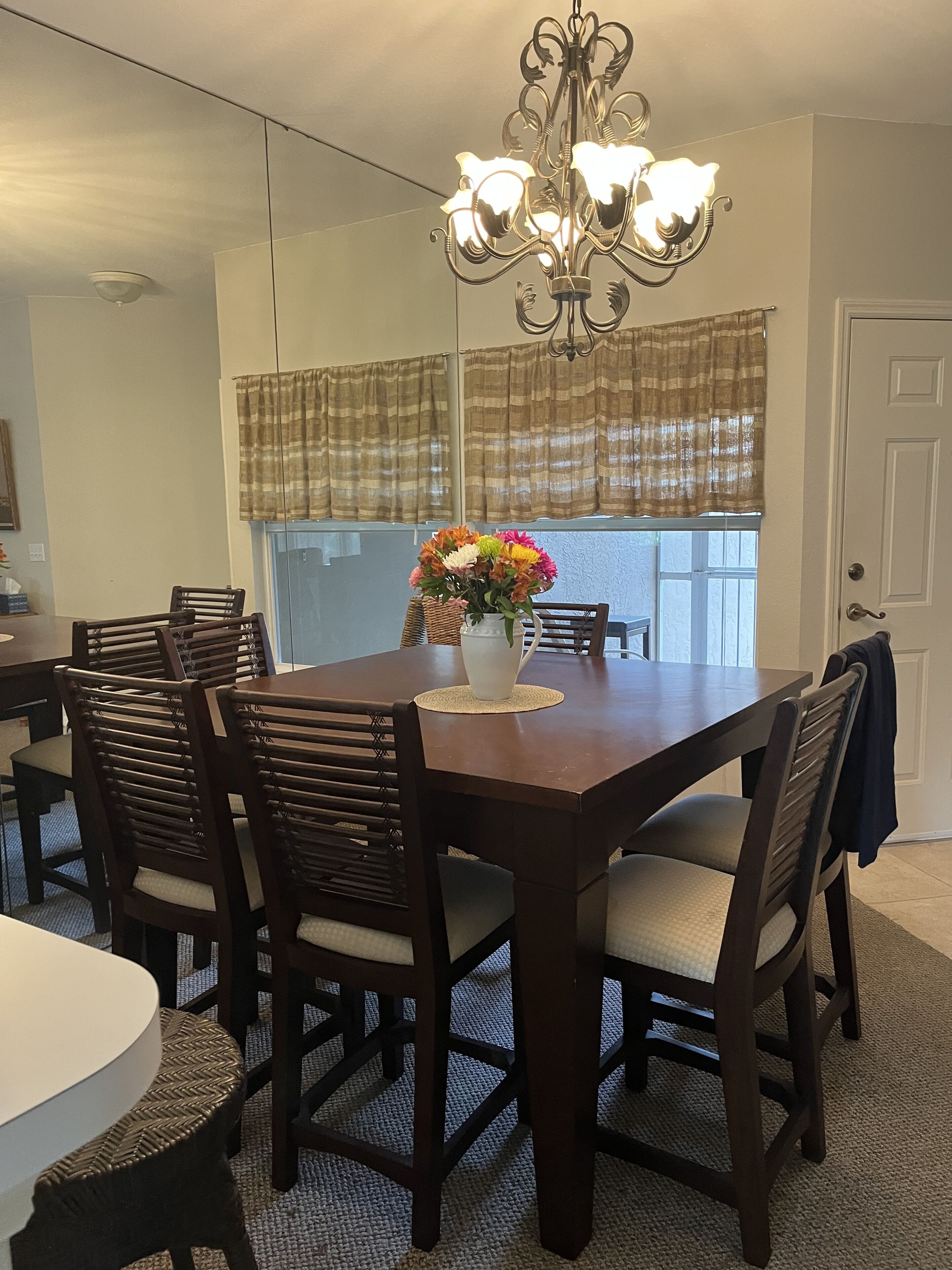 A dining room with a wooden table, six chairs, a chandelier, and a vase with flowers.