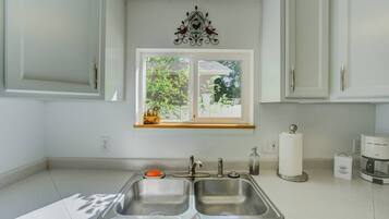 Una cocina con un lavamanos doble, una ventana que da a vistas de vegetación y un adorno metálico sobre la ventana.