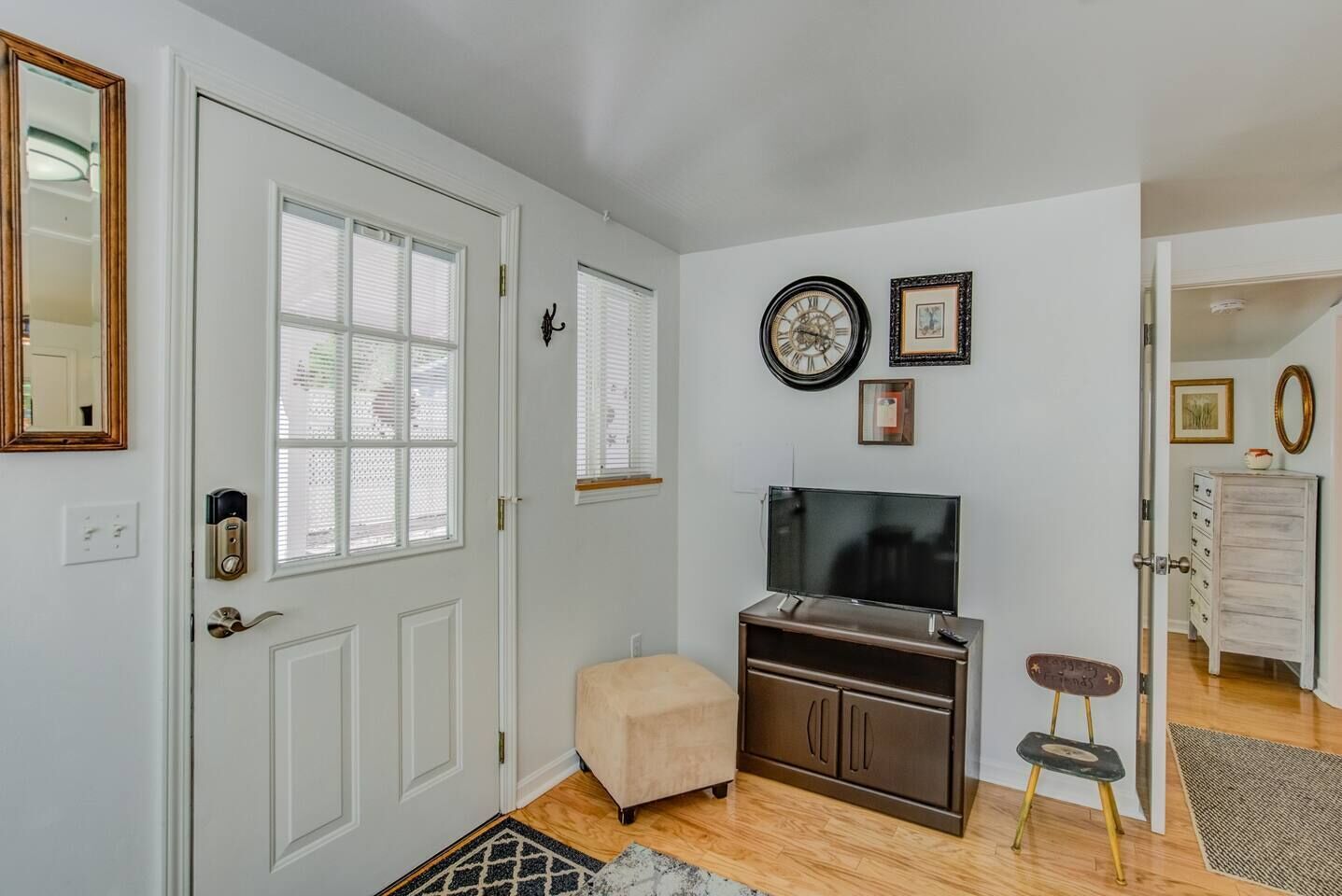 A hallway with a white door, a television on a cabinet, a small stool, and a rug.