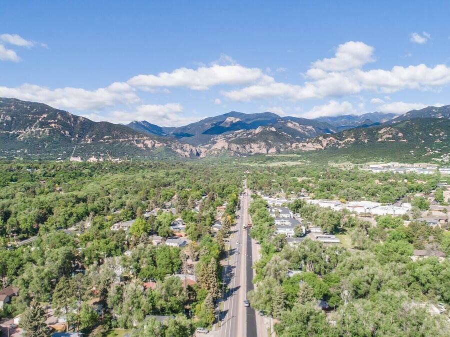 A residential area with a road leading towards distant mountains, surrounded by dense greenery and residential buildings.