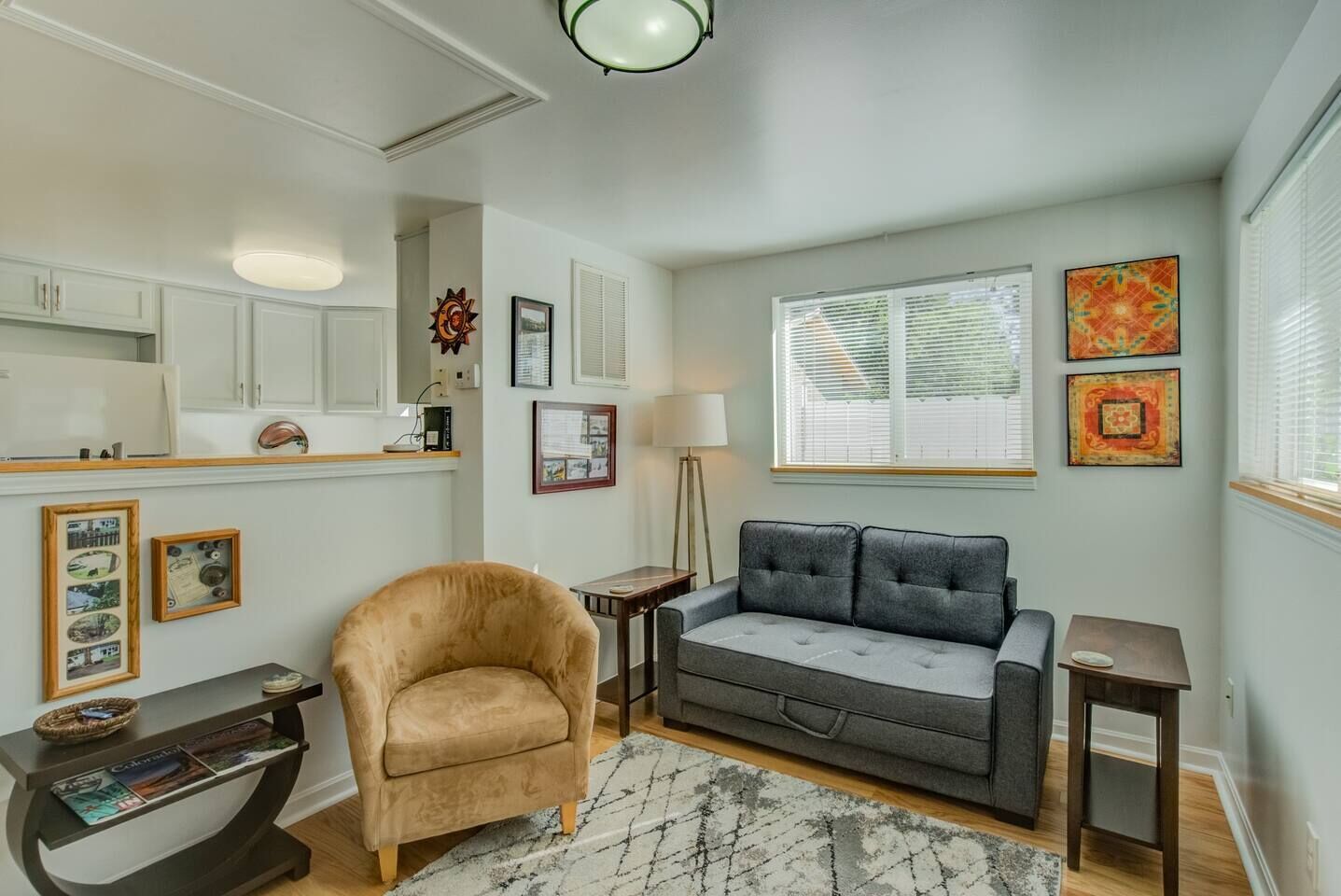 A living room with a beige armchair, a grey sofa, a small table, and a wall-mounted shelf.