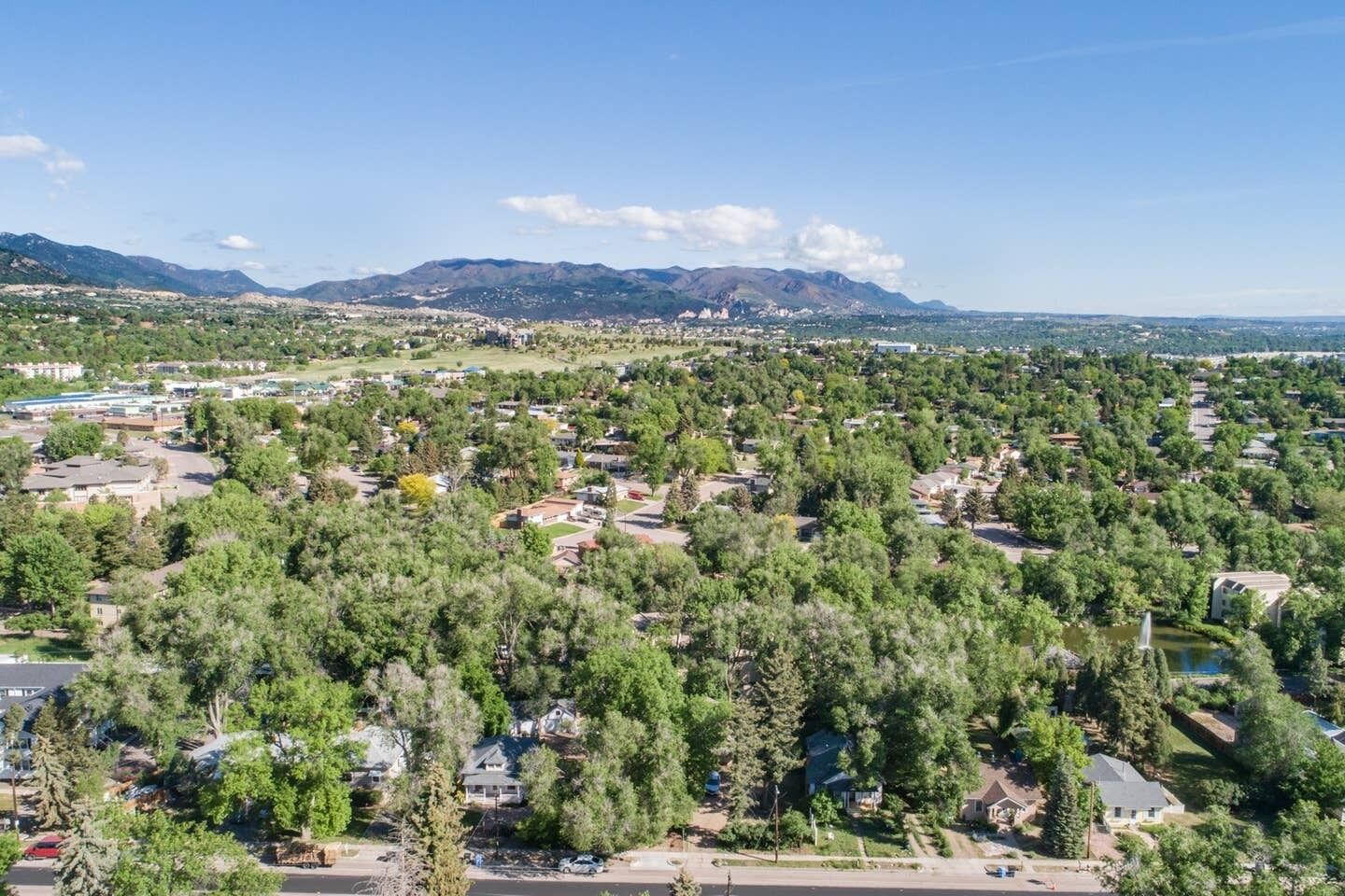 A residential area with houses surrounded by dense trees and a mountain range in the background.