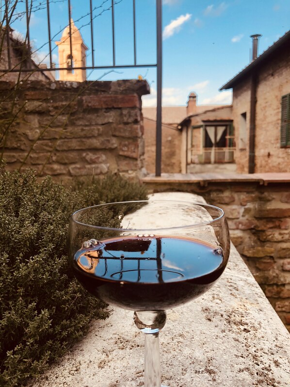 A glass of red wine on a stone ledge with a stone wall and a building in the background.