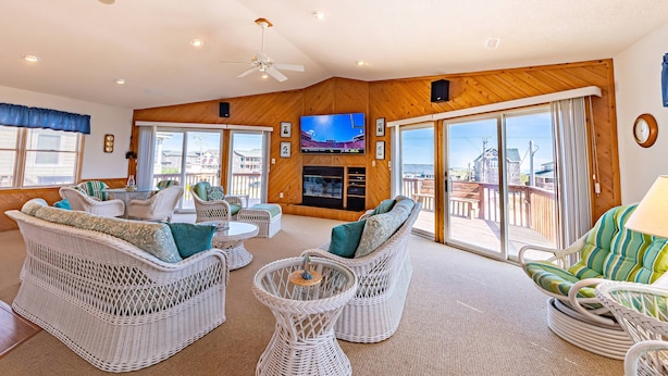 A spacious living room with wicker furniture, a flat-screen TV, and a balcony with a view.