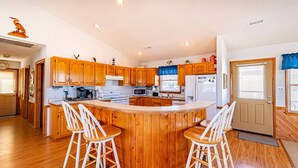 A kitchen with wooden cabinets, a central island with stools, a refrigerator, microwave, and coffee maker.