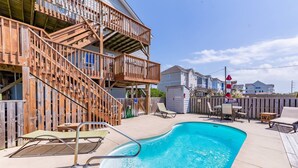 A swimming pool with a wooden deck, lounge chairs, and a staircase leading to a balcony.