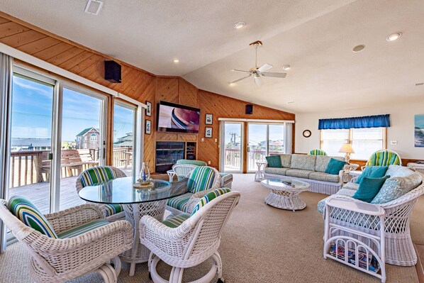 A spacious living area with wicker furniture, a glass-top coffee table, and a television mounted on the wall.