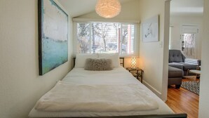 Ett sovrum med en säng, ett fönster, en hängande lampa och en tavla på väggen.