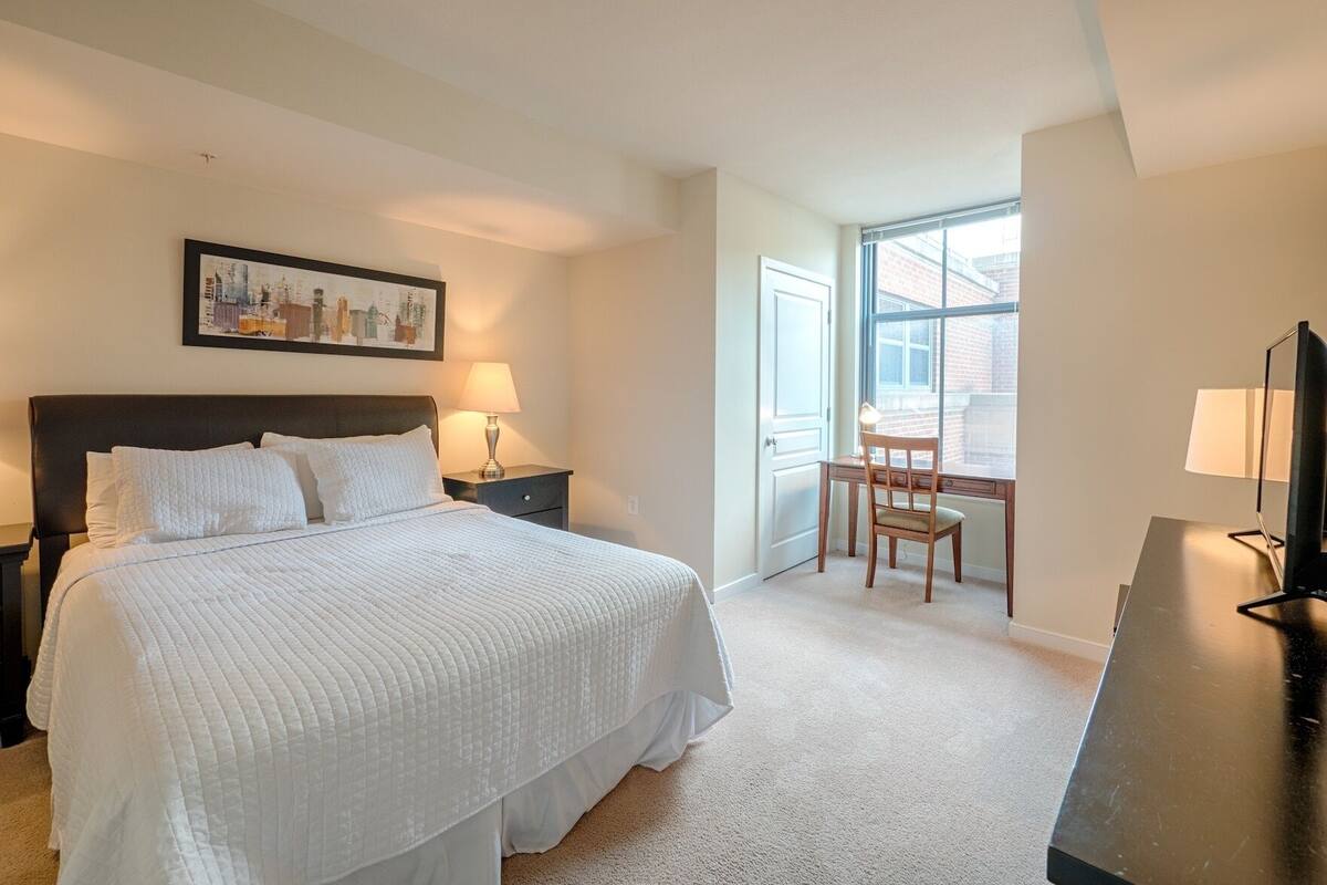 A hotel room with a large bed, a desk, a chair, and a television.