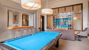 A pool table with stools, a bar area, and a seating area with a TV. - National at Metropolitan Park (Arlington)