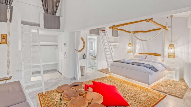 Un dormitorio con cama, una escalera, cabecera de madera y un baño visible a través de una puerta abierta.