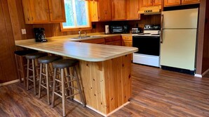 Una cocina con armarios de madera, una isla central con taburetes, microondas, estufa y refrigerador.
