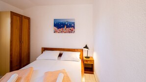 A neatly made bed with white linens, a wooden headboard, and a nightstand with a lamp.