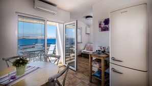 A compact kitchen with a white refrigerator, a dining table with chairs, and a view of the sea through large windows.
