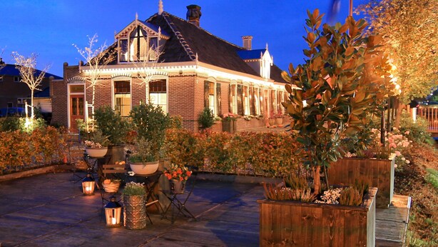 A traditional brick building with a steep roof and dormer windows, surrounded by well-maintained gardens and outdoor seating areas. - Hotel Suites Wilma J (Vinkeveen)