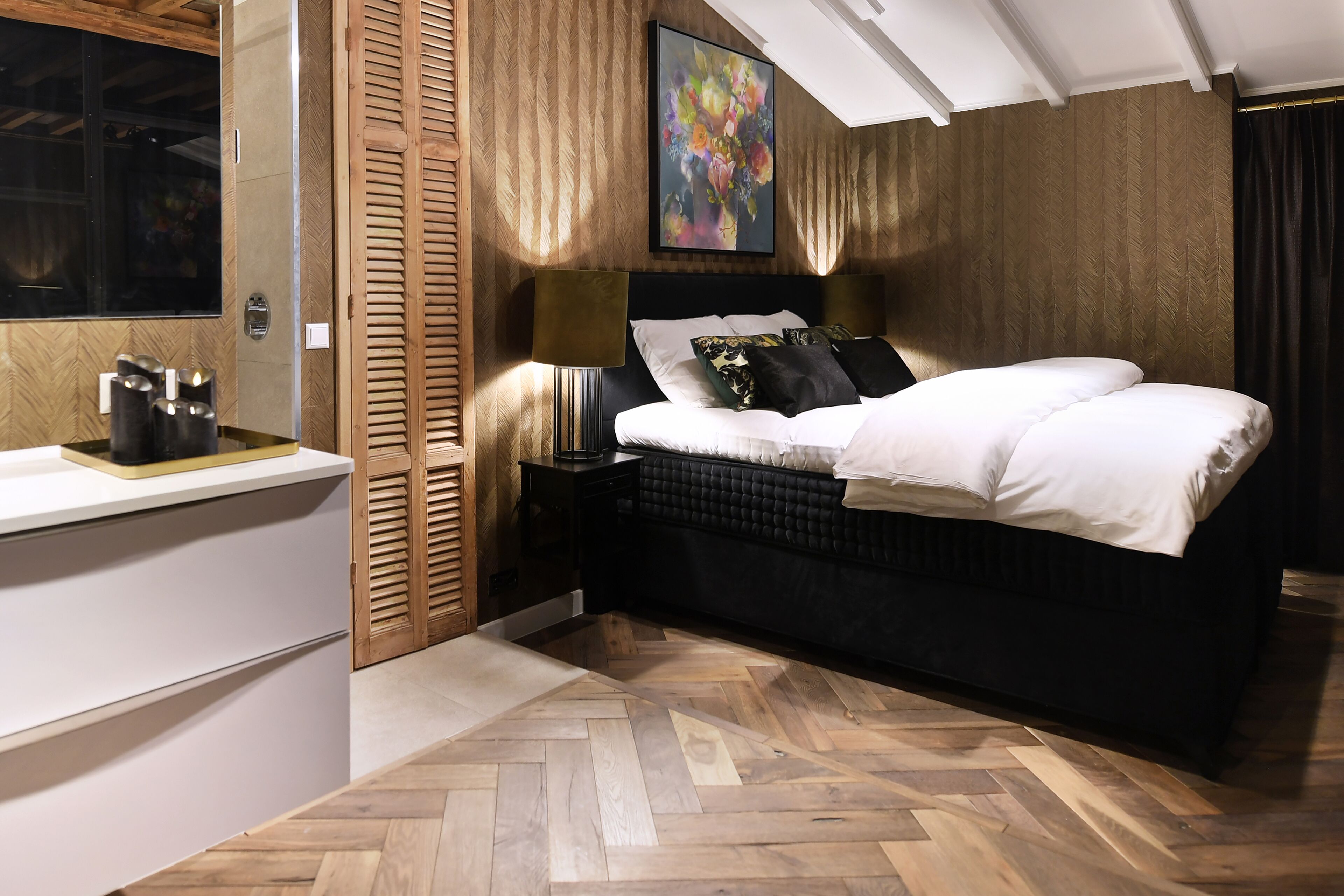 Een slaapkamer met een bed, nachtkastje, lamp en een schilderij aan de muur.