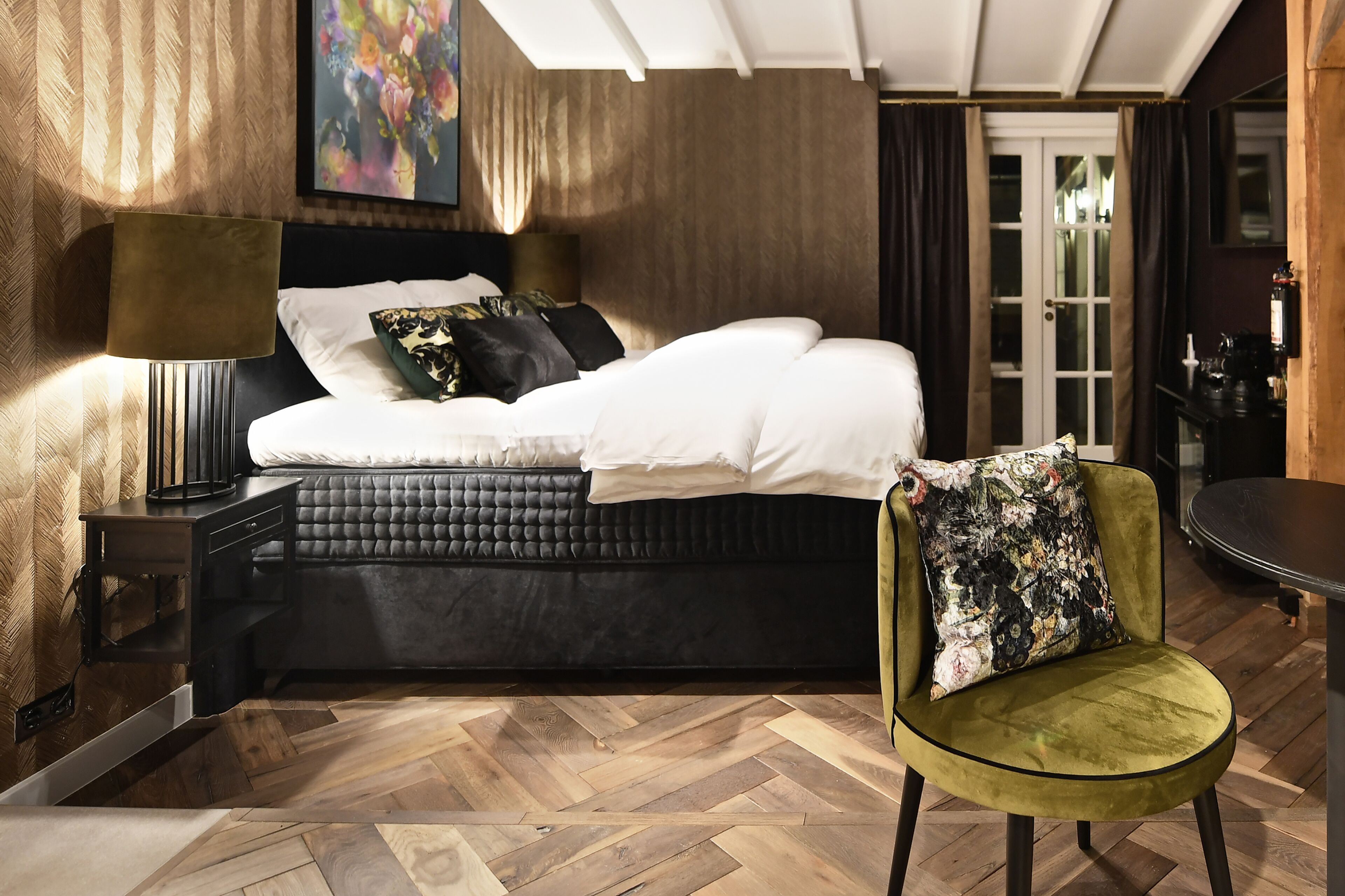 A modern bedroom with a bed, a green chair, a nightstand, and a lamp.