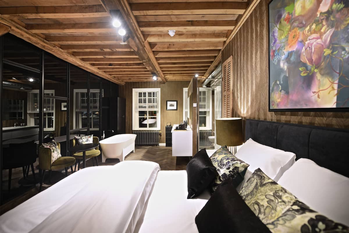 Une chambre d’hôtel avec un grand lit, un coin salon avec une table et des chaises, un grand miroir et un tableau au mur.