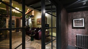 A modern interior with a herringbone wood floor, a dark-colored sofa, a green side table, and a spiral staircase. - Hotel Suites Wilma J (Vinkeveen)