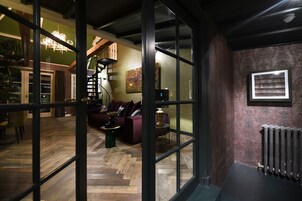 Um interior moderno com piso de madeira em padrão herringbone, um sofá de cor escura, uma mesinha lateral verde e uma escada em espiral.
