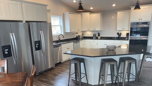 Una cocina moderna con electrodomésticos de acero inoxidable, armarios blancos y una isla central con taburetes de bar.