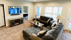 Una sala de estar con un amplio sofá modular, un televisor de pantalla plana montado en la pared, una mesa de centro y una mesita auxiliar.