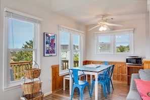 Relax in this spacious living area with a dining table, sofa, and bench, offering views of the outdoors through large windows.