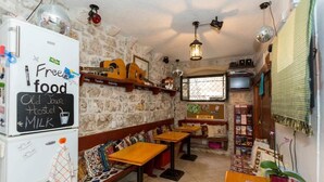 A cozy hostel room with a chalkboard sign advertising free food and milk, wooden benches, a small TV, and a stone wall.