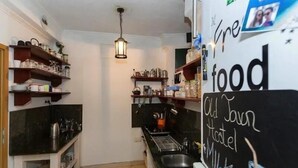 A compact kitchen with shelves holding various kitchenware, a hanging light fixture, and a chalkboard with handwritten text.