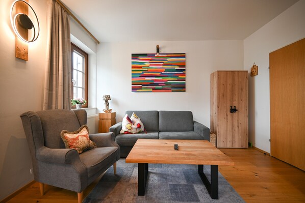 A living room with a grey sofa, a wooden coffee table, and a colorful abstract painting on the wall.
