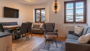 Ein modernes Wohnzimmer mit Esstisch aus Holz, grauen Sofas und einem an der Wand montierten Fernseher.