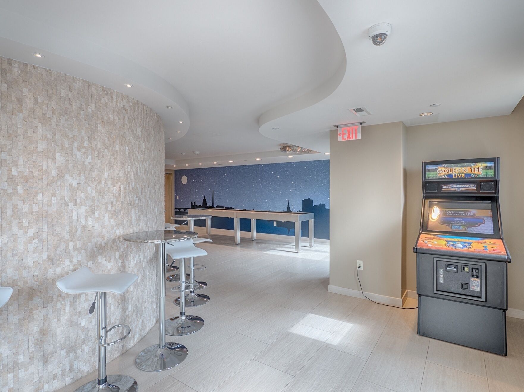 A modern bar area with a pool table, bar stools, and a gaming machine.