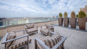 Een terras op het dak met gestreepte fauteuils met kussens en plantenbakken, met uitzicht op een stadsgezicht.