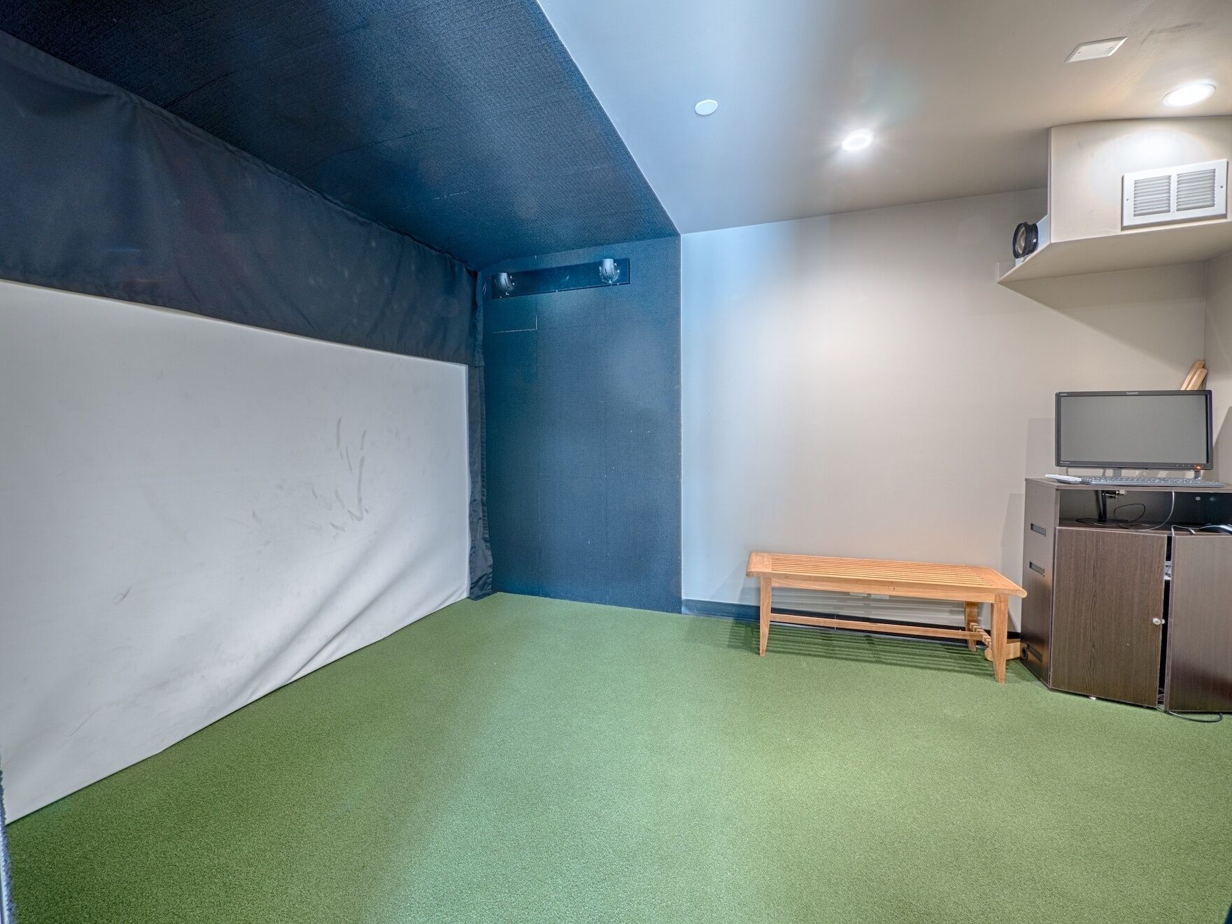 A room with a green carpet, a white wall, a dark blue wall, a wooden bench, a desk with a computer, and a TV.