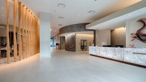 Eine moderne Hotelhalle mit einer Rezeption, einer gewölbten Wand mit Marmorverkleidung und einer Säulenstruktur aus Holz.
