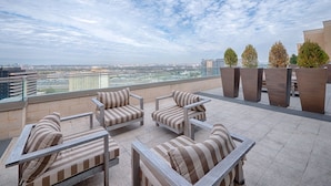 Eine Dachterrasse mit gestreuten Sitzmöbeln und Pflanzgefäßen mit Blick auf eine Stadtlandschaft.
