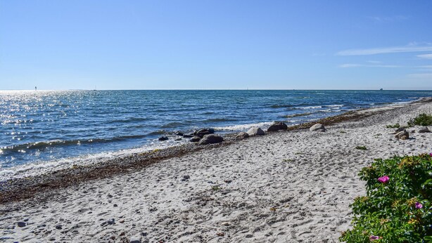 Une plage bordée d’une côte rocheuse, avec une eau d’un bleu limpide et un navire visible au loin.
