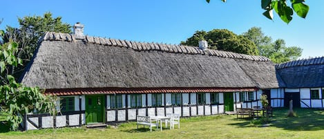 A traditional thatched-roof house with a white and black half-timbered facade, a green door, and a small outdoor seating area.