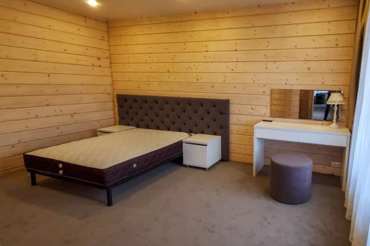 A bedroom with a bed, a desk, a chair, and a small stool.