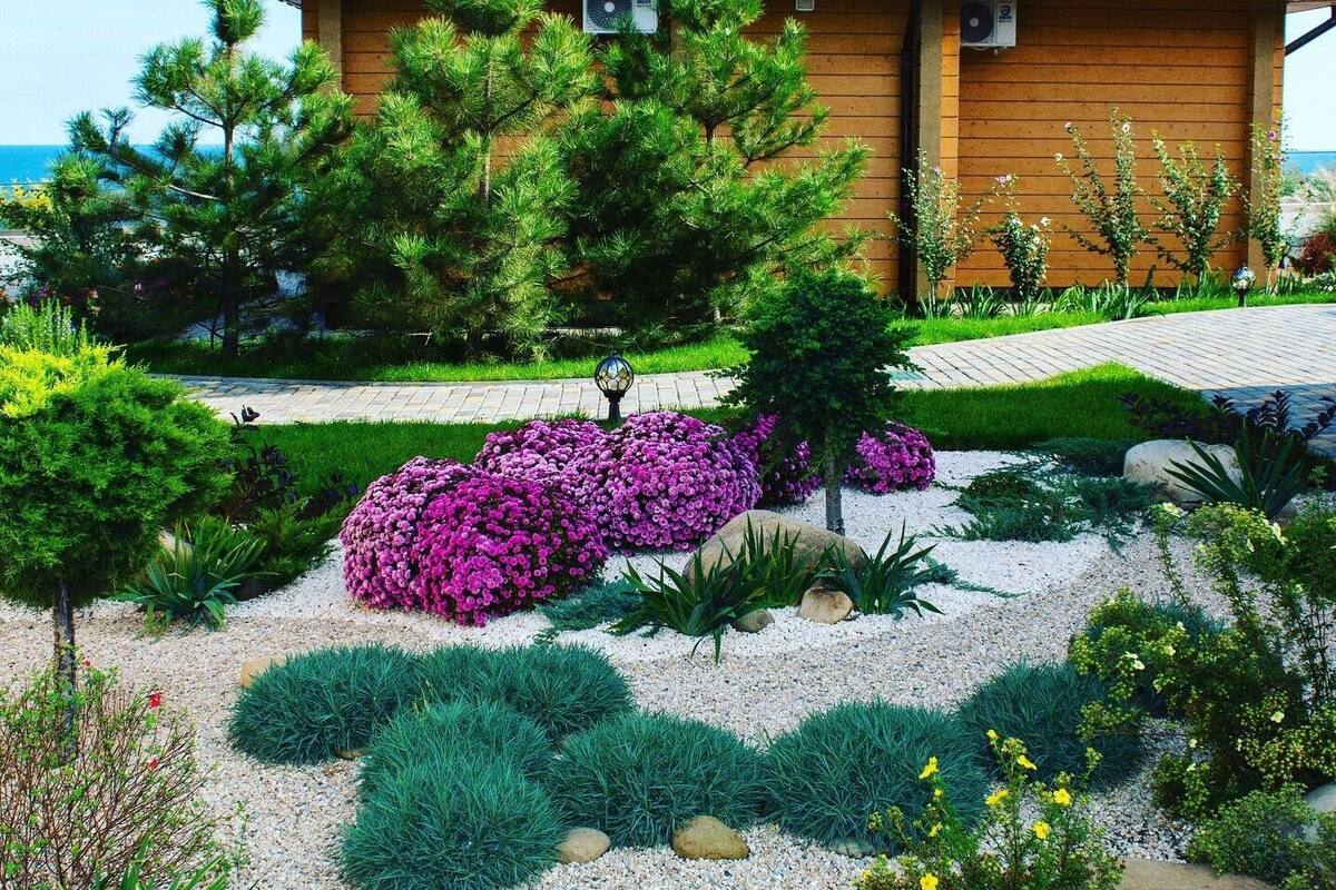 A house with a sloped roof, surrounded by a well-maintained garden with various plants and flowers.